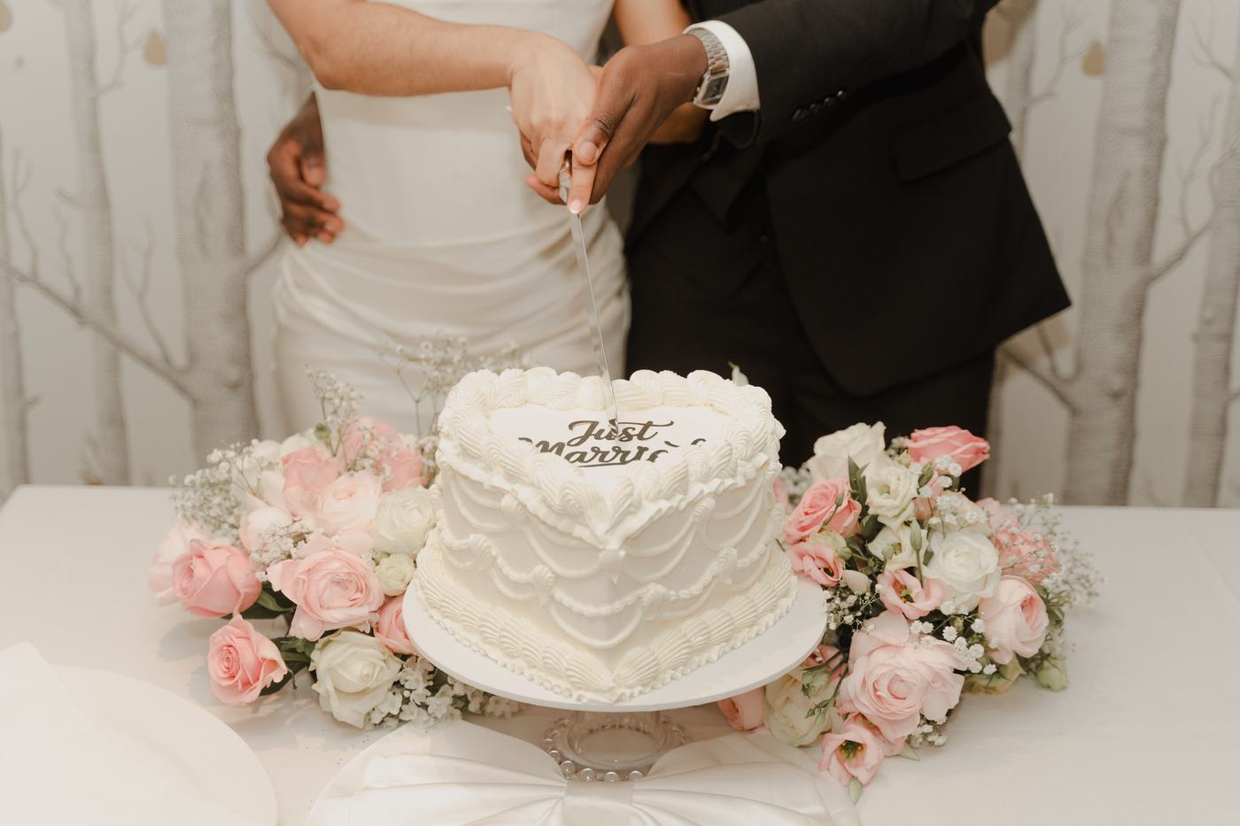 Couple cutting a white heart-shaped Just Married cake surrounded by pink and white roses